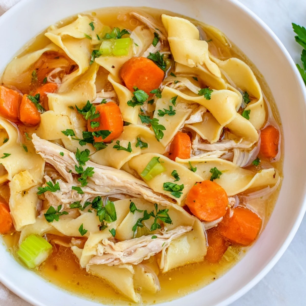 Steaming, golden Cozy Chicken Noodle Soup served in a bowl, with herbs and carrots visible.