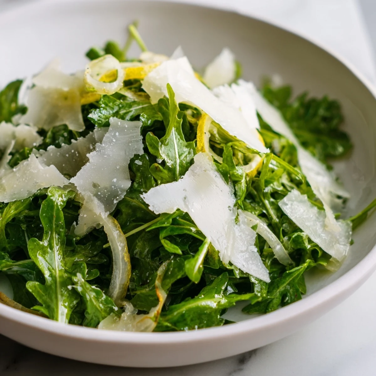 Bright, green arugula salad with lemon dressing, topped with shaved Parmesan cheese ready to enjoy.