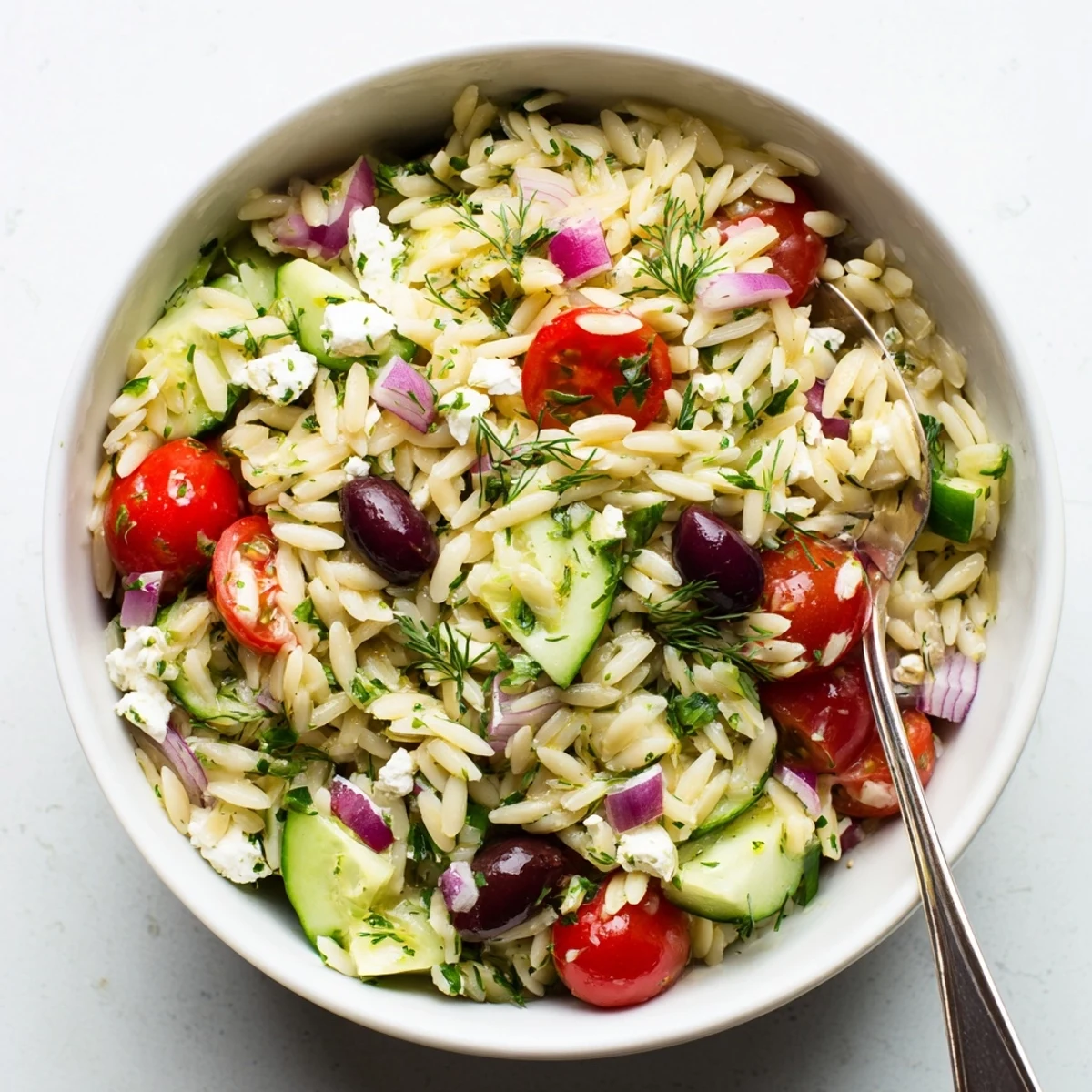 Close-up of a vibrant Greek Orzo Salad featuring tender pasta, diced cucumbers, halved cherry tomatoes, and crumbled feta cheese tossed in a zesty lemon-oregano dressing.