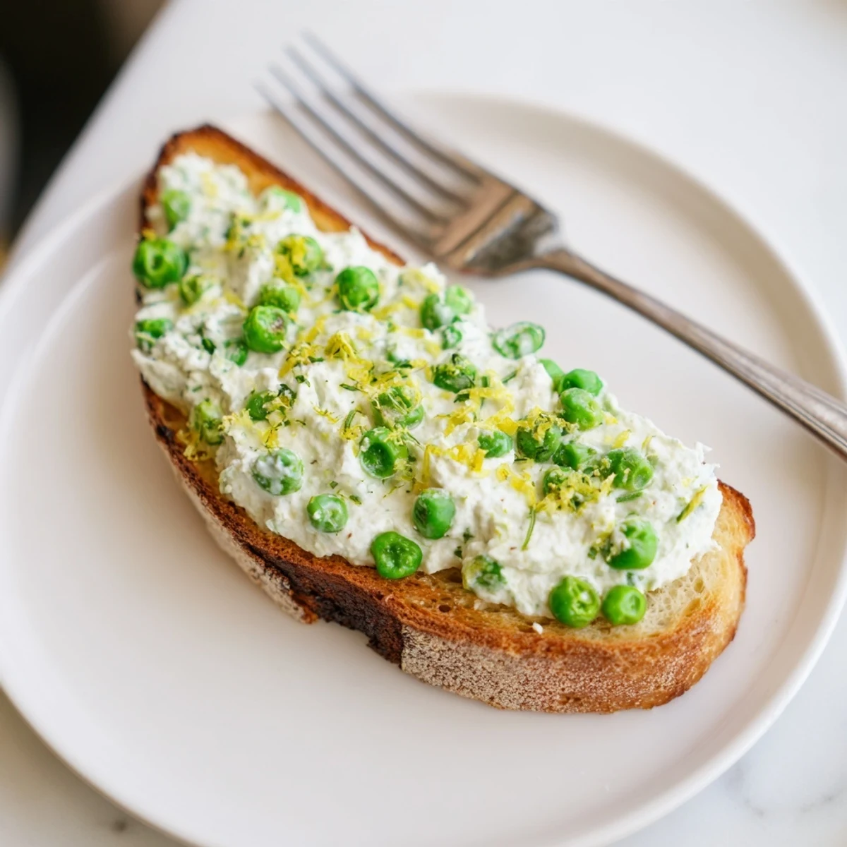Savory pea and mint ricotta spread on crunchy toast, finished with olive oil drizzle and lemon wedges for serving.