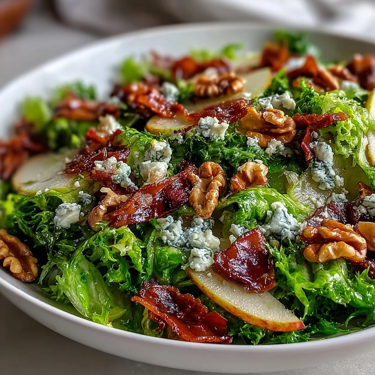 An overhead shot of Frisée, Pear, Blue Cheese, and Crispy Prosciutto Salad, with crisp prosciutto pieces, pear slices, and a drizzle of tangy vinaigrette over greens.