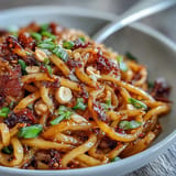Chewy wheat noodles tossed with chili crisp, garlic, and soy sauce, topped with fresh scallions and optional bean sprouts.  