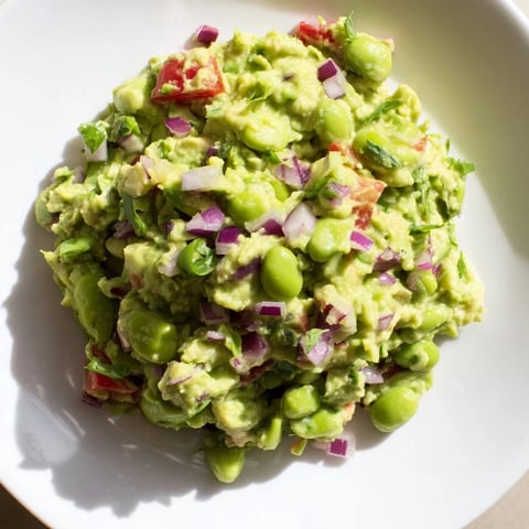 Vibrant green Edamame Guacamole, a creamy dip with visible chunks of red onion and tomato.
