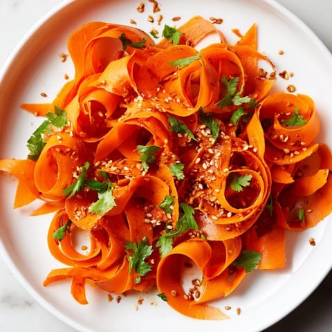 A close-up of the vibrant Carrot Ribbon Salad Asian-Style, featuring crisp carrot curls and fresh cilantro garnish on a white plate.  