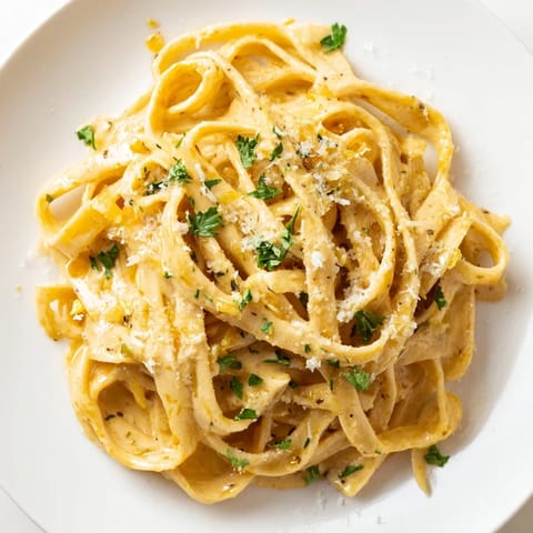 A skillet of Sriracha Honey Pasta steam gently, featuring plump noodles drenched in a spicy-sweet garlic butter cream sauce.
