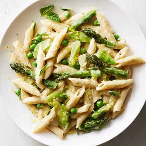 Overhead view of a white bowl filled with fresh Garlic Parmesan Spring Vegetable Pasta, garnished with extra Parmesan and chopped basil leaves, on a rustic wooden table.