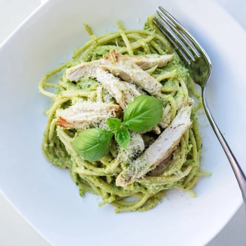 A close-up of creamy avocado chicken pasta tossed in a luscious green sauce, garnished with lemon zest and basil.