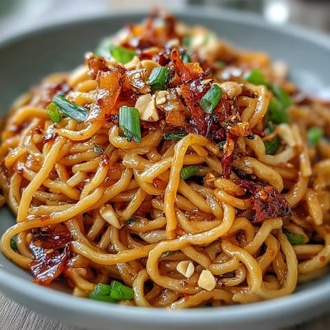 Spicy chili crisp noodles in a bowl, garnished with scallions and roasted peanuts for a crunchy, savory bite.  