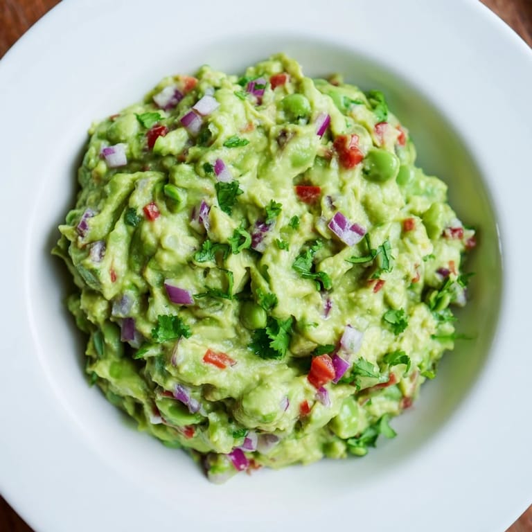 A close-up of chunky Edamame Guacamole, ready to be scooped up with crispy tortilla chips.