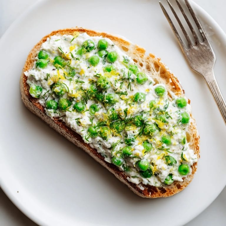 A vibrant slice of pea and mint ricotta toast, garnished with fresh mint and lemon, ideal for a quick vegetarian brunch.  