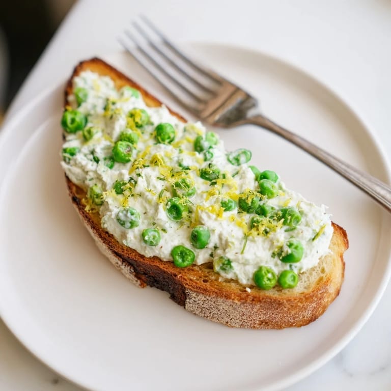 Savory pea and mint ricotta spread on crunchy toast, finished with olive oil drizzle and lemon wedges for serving.