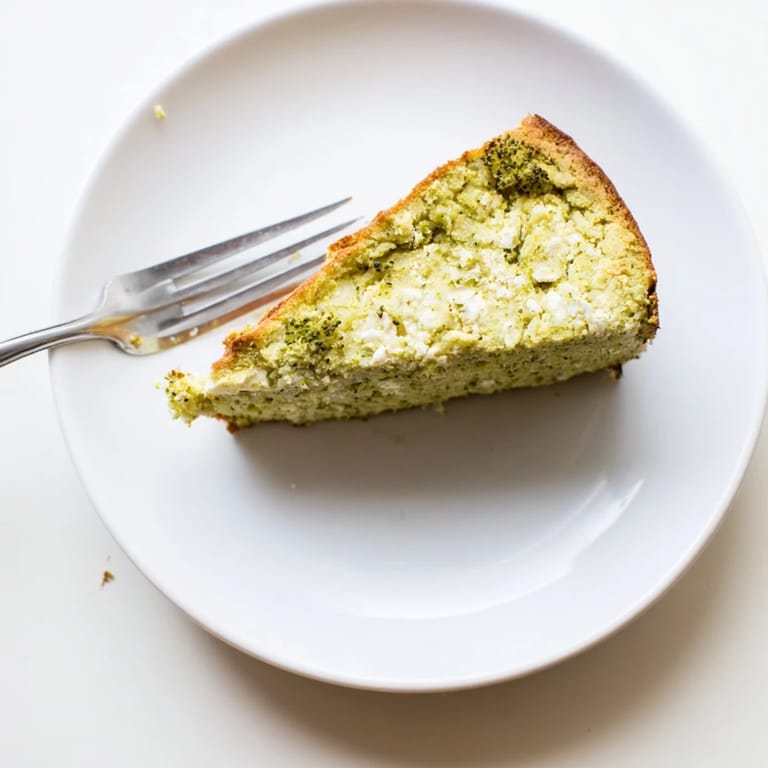 Homemade Mediterranean-style broccoli and feta loaf in a parchment-lined pan, cooled and cut to show its soft, moist crumb.