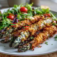 Golden-brown Crispy Parmesan Asparagus Chicken Salad piled high on a white platter, topped with cherry tomatoes and fresh basil.
